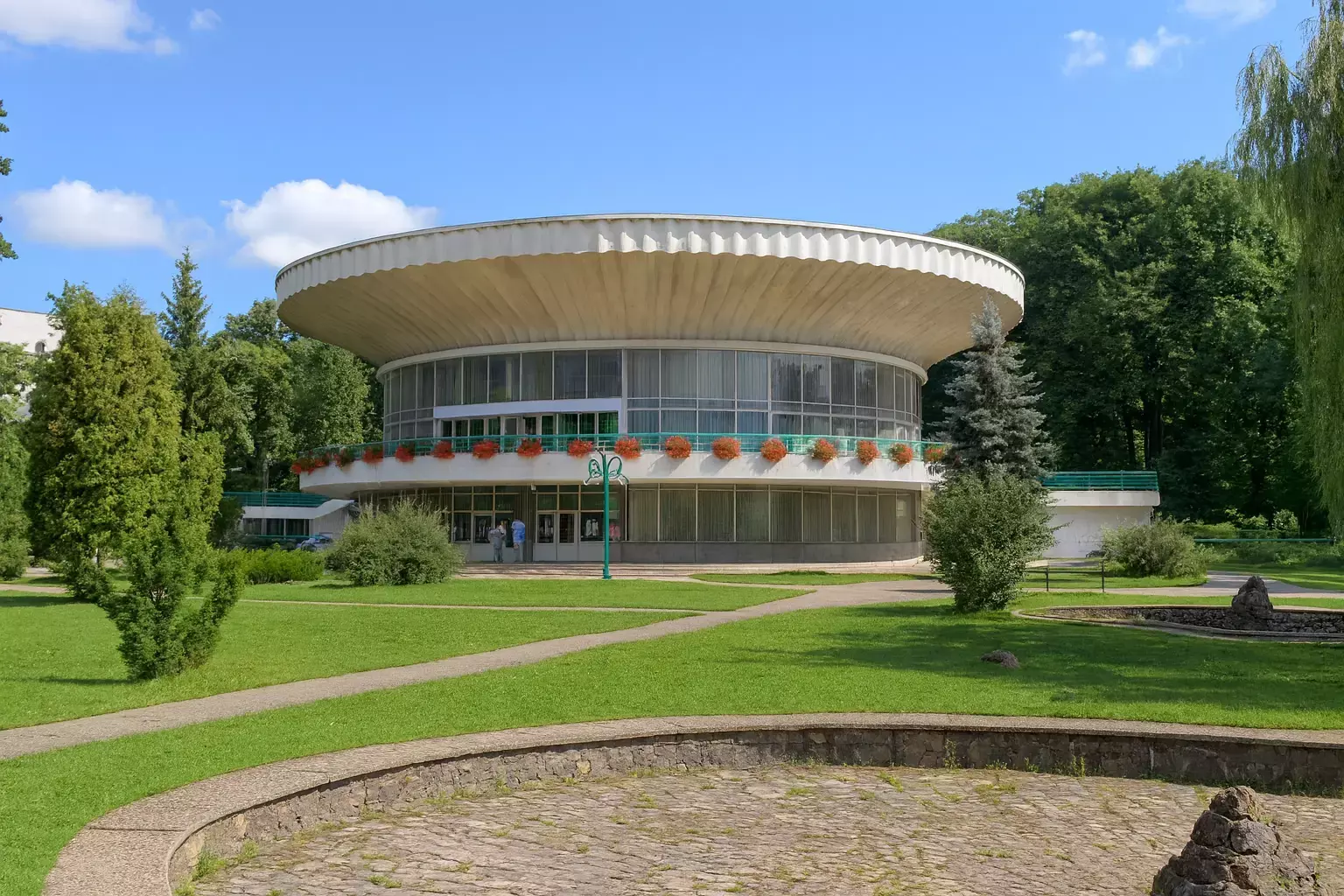 Pavilionul de apă minerală din Morshyn cu o clădire modernistă rotundă situată în mijlocul unui parc verde.        